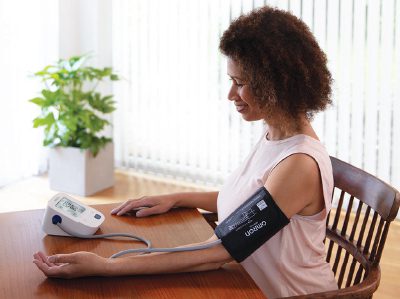 Imagen de una mujer con un monitor omron bronze de color blanco para medir presión arterial.